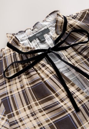 Brūna un bēša pledveida blūze ar volāna apkakli, melnu samta tauriņu un savākta tekstūra pie kakla līnijas. Iekšpusē redzama etiķete.