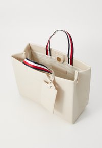 Beige tote-väska tillverkad av syntetiskt material med dubbla handtag i rött, vitt och svart randigt mönster samt en sidetikett. Har ett rymligt insida.