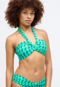 Zaļš rakstains bikini komplekts, kas sastāv no bandeau topa ar savītu priekšpusi un kakla siksnu, apvienots ar zemu vidukļa apakšdaļu. Gluda auduma tekstūra.