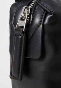 Černá kožená kabelka s kovovým zipem, značkou CK a texturovaným povrchem. Obsahuje koženou nášivku s precizním šitím.