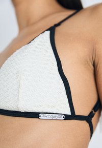 Driehoek bikini-top gemaakt van gestructureerde witte stof met zwarte rand. Voorzien van een zilveren logo-label en slanke verstelbare bandjes.