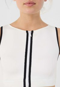 Top bianco aderente con scollo rotondo, con bordo intrecciato nero lungo i bordi e zip frontale. Texture liscia.