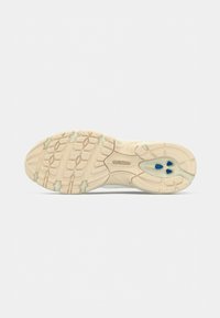 Semelle d'une chaussure New Balance beige avec un motif de bande de roulement texturé et des accents bleus sur la zone du talon.