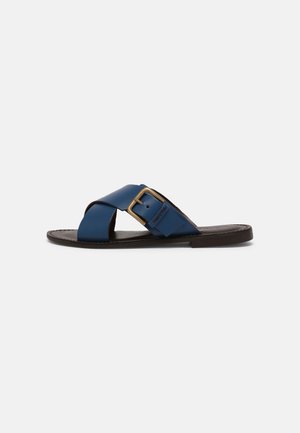 Blue leather slide sandal with a cross-strap design, featuring a gold metal buckle and a brown sole. Smooth texture and minimal detailing.