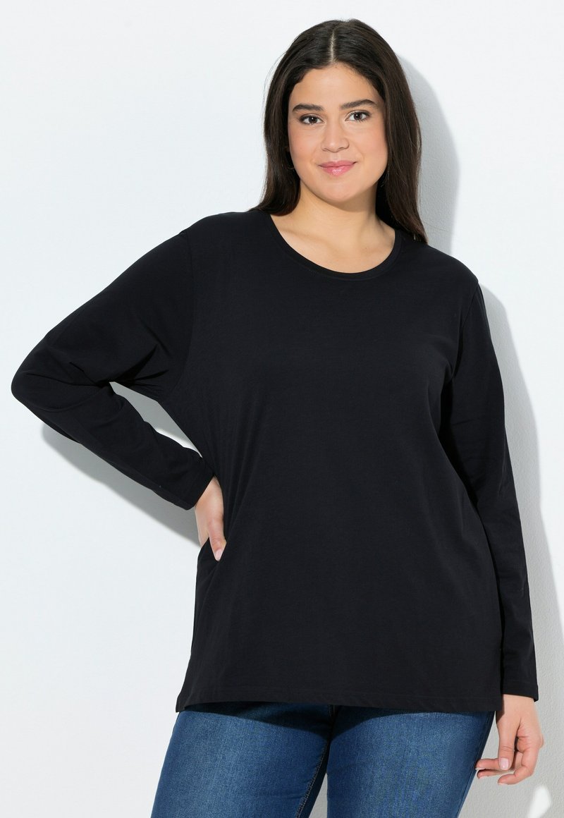 Schwarzes Langarmshirt aus weichem Stoff mit rundem Halsausschnitt und lockerer Passform. Kombiniert mit blauen Jeans, die eine glatte Textur aufweisen.