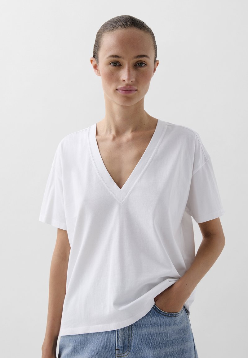 Witte katoenen T-shirt met een diepe V-hals en korte mouwen, met een ontspannen pasvorm en een schoon, minimalistisch ontwerp. G gedragen met spijkerbroeken.