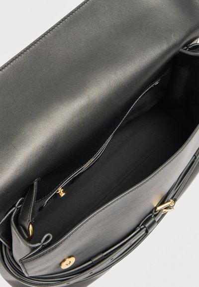 Sac à main en cuir noir ouvert montrant un intérieur lisse, une poche zippée, et des détails en bouton et boucle dorés.
