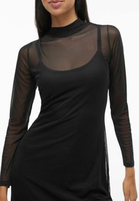 Melnas kleitas ar garām caurspīdīgām tīkla piedurknēm, augstu apkakli un piegulošu augšdaļu, raksturota ar gludu tekstūru un sānu šķēlumiem papildus detaļām.