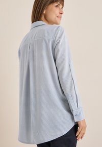 Camicia a righe blu e bianche con colletto, maniche lunghe, dettagli di pieghe posteriori e polsini abbottonati. Tessuto morbido.