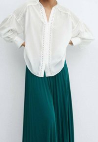 Witte blouse met pofmouwen, kantdetails en knoopsluiting, gecombineerd met een lange, geplooide teal rok. Zachte stof en een ontspannen pasvorm.