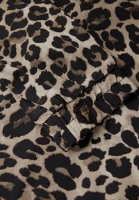 Látka s leopardím vzorem, která zobrazuje béžové pozadí s černými a tmavě hnědými skvrnami. Materiál se zdá být měkký s hladkým povrchem.