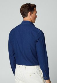 Camicia blu navy a maniche lunghe con colletto su misura e yoke posteriore, caratterizzata da una vestibilità rilassata e dettagli di cucitura discreti.