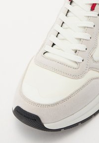 Sneaker grigio chiaro con pannelli in pelle e suede bianca. Presenta lacci bianchi, cuciture a vista e una suola in gomma nera testurizzata.