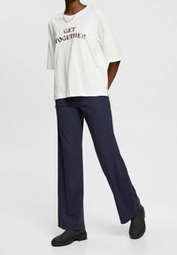 Camiseta de algodón blanca de gran tamaño con "GET TOGETHER" impreso en letras metálicas; combinada con pantalones de pierna ancha de color azul oscuro y botas negras.
