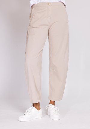 Beige straight-leg pants paired with white low-top sneakers on a person standing against a plain backdrop.