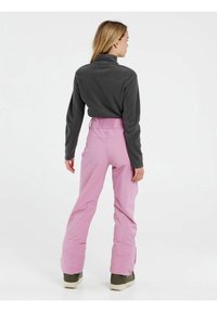 Grijs fleece top met hoge kraag gecombineerd met roze skibroeken, met een trekkoord in de taille en een relaxte pasvorm, gedragen met groene sneeuwlaarzen.