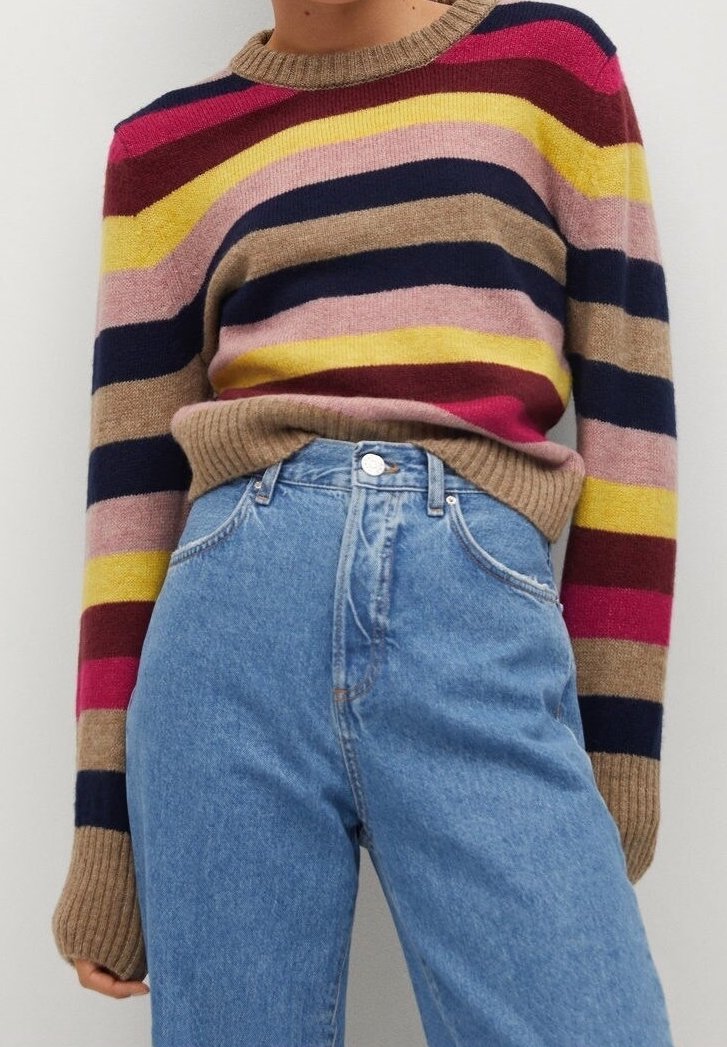 Persona con un suéter de rayas multicolores, con puños y cuello beige, metido dentro de unos jeans de tiro alto de color azul claro.