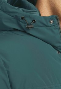 Tirkizna izolirana jakna s kapuljačom na mašnicu, zatvaranjem na zip i dugmadima na klik. Glatka tekstura tkanine s blagim sjajem.