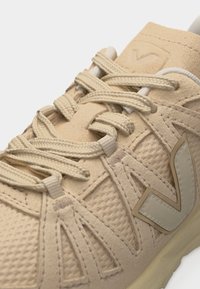 Baskets beiges avec une maille texturée et des superpositions en daim, des lacets épais beiges, et un grand logo "V" sur le côté.