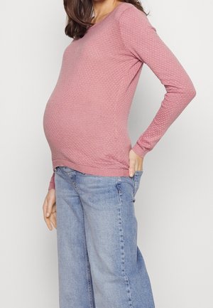 Haut en maille texturée rose à manches longues, associé à un jean large bleu clair. Le haut présente un col rond et un ourlet côtelé.