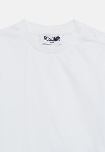 Λευκό παιδικό μπλουζάκι με ριμπ λαιμόκοψη, κουμπιά με πατιλέτα στον ώμο και ετικέτα Moschino Baby ραμμένη μέσα στον γιακά.