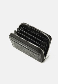 Portefeuille en cuir noir avec un motif texturé, fermeture éclair en argent et plusieurs compartiments pour cartes et billets. Logo en relief sur le devant.