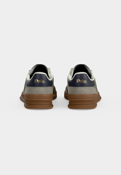 Ζευγάρι γκρι και σκούρα μπλε αθλητικά Polo Ralph Lauren, ορατά από πίσω, με καφέ σόλες και χρυσό λογότυπο στο πίσω μέρος του αστραγάλου.