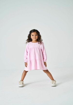 Roze tiered jurk met lange mouwen, gemaakt van geweven stof, gecombineerd met beige sneakers. De jurk heeft een ontspannen pasvorm en een ronde halslijn.