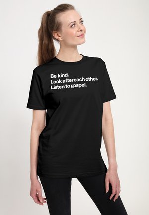 Sort T-shirt med hvid tekst: "Vær venlig. Pas på hinanden. Lyt til gospel." Standard pasform med korte ærmer og rund hals.
