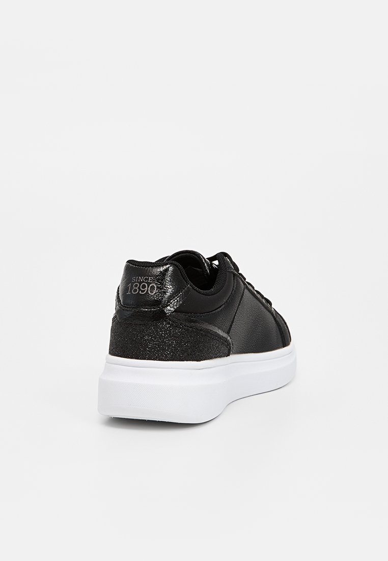 Baskets noires avec une finition en cuir lisse, accent pailleté au talon, semelle blanche et forme arrondie. Présente "SINCE 1890" à l'arrière.