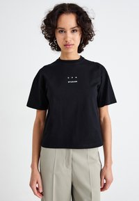 Zwarte katoenen t-shirt met een ronde hals en korte mouwen. Kenmerkt zich door witte tekst "CPH STUDIOS" op de voorkant, met een losse pasvorm.