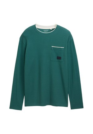 Camisa verde de manga larga con ribete blanco en el cuello y el bolsillo del pecho, que presenta una pequeña etiqueta oscura en el bolsillo.