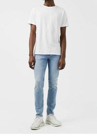 Vit bomull T-shirt i kombination med ljusblå slim-fit jeans och vita sneakers. Outfiten har en klassisk design och enkla färger.