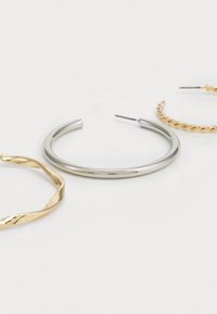 Drie paar oorringen: een gedraaid gouden ontwerp, een gladde zilveren band en een gevlochten gouden optie met een slanke pin sluiting.