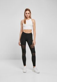 Sorte leggings med gjennomsiktige paneler, tettsittende design, høy midje, kombinert med en hvit kortermet tank topp. Hvite treningssko fullfører antrekket.