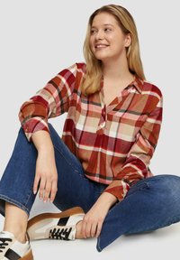 Rood en beige geblokt overhemd met lange mouwen, button-down kraag en een ontspannen pasvorm, gecombineerd met blauwe denim en witte sneakers.