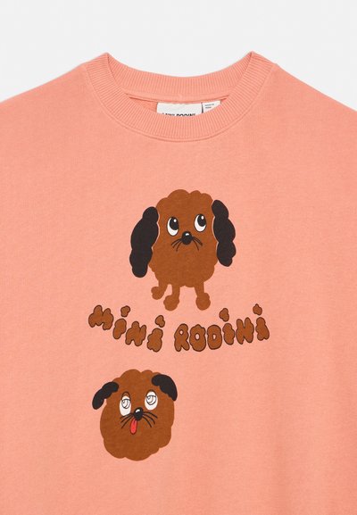 Sweat-shirt rose clair avec deux chiens marron de dessin animé aux oreilles noires et aux yeux expressifs, avec le texte "mini rodini" en lettres marron stylisées.
