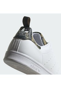 Adidas Stan Smith-sneakers med övre del i vitt läder, hälen med kamouflagemönster och en strukturerad gummisula med varumärkeslogotyp på baksidan och sidan.