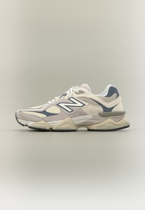 Baskets New Balance beige clair et grises avec panneaux en mesh et daim, semelle épaisse et coussinée, et grand logo "N" sur le côté.