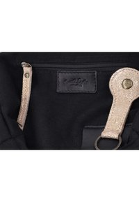 Intérieur en tissu noir d'un sac avec une poche zippée, une lanière en cuir beige pailletée avec un bouton-pression métallique et un porte-clés, ainsi qu'une étiquette de marque noire.