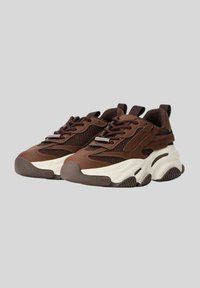 Sneaker multi-material marrone con suola chunky, dettagli in rete, chiusura con lacci e branding sottile sui lati, caratterizzati da una texture rigata.
