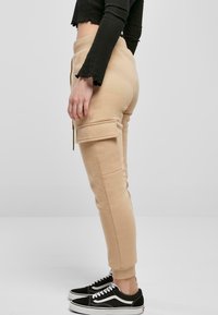 Beige cargo kalhoty s tapered nohavicemi, se bočními kapsami a měkkou, texturovanou tkaninou. Spárovány s černými teniskami a zkráceným topem.