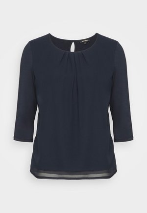 Mørkeblå bluse med trekvartlange ærmer, rund halsudskæring, folder foran og en lille nøglehulsknaplukning bagpå.