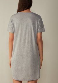 Vestido de camiseta de algodón gris con mangas cortas, corte relajado y cuello redondeado, con una textura suave y un dobladillo ligeramente curvado.