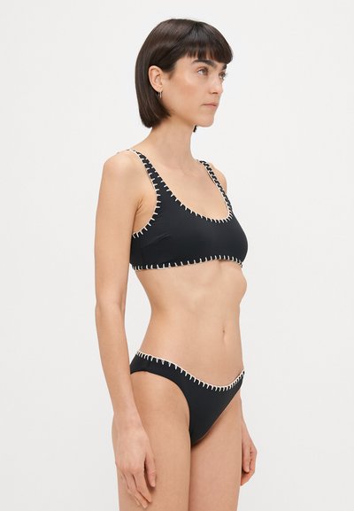 Svart bikinitopp med hvite sømmer. Toppdelen har en vid halslinje og tynne stropper; bunnen er lavt liv med matchende sømmer.