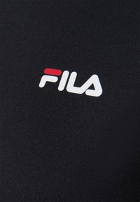 Černá textilie s vertikálním žebrováním, vyznačující se bílým logem "FILA" zvýrazněným červenými a modrými prvky.