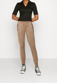 Joggers en suède beige avec des poignets élastiques et une taille à cordon, associés à un polo noir cintré à manches courtes en côte et des baskets montantes noires.