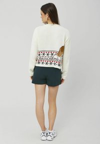 Pull en tricot crème avec un design à motifs représentant un chien, agrémenté de cœurs rouges et de nœuds, associé à un short vert foncé.