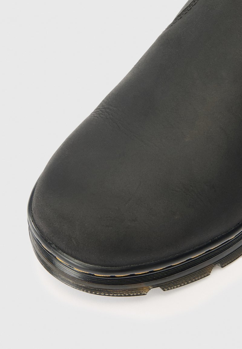 Gros plan sur l'orteil d'une botte en cuir noir avec une semelle texturée et des coutures visibles le long du bord de la semelle.