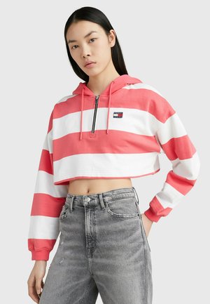 Hoodie accorciato a righe corallo e bianche, con zip frontale e cappuccio. Abbinato a jeans grigi a vita alta con una texture strappata.